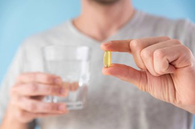 Beslenme takviyeleri. İnsan ve elinde bir bardak suyla Omega 3 kapsülü tutuyor. Sabah dozunda vitamin. Haplı balık yağı. Sağlık hizmeti kavramı