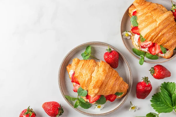 stock image French croissant sandwich with fresh ripe strawberries and cream cheese in a plate with flowers on white background. top view with copy space. tasty breakfast