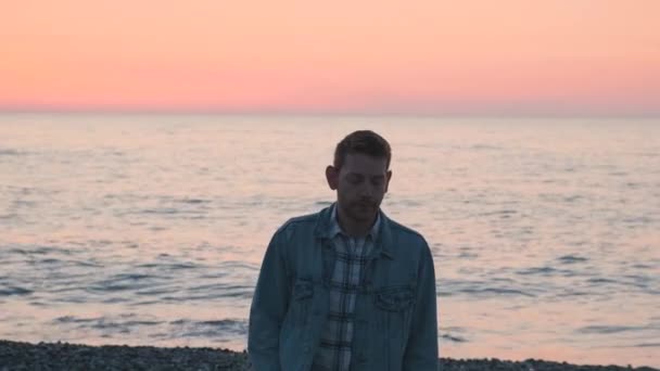 若い白人男性は日没に一人で海岸を歩いている 海のそばのビーチで思慮深い男 シフトフォーカス うつ病 憂うつなストレスの概念 — ストック動画