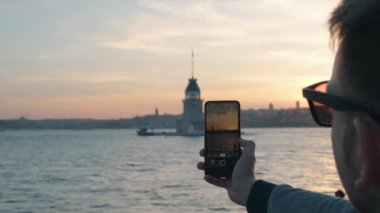 İstanbul Boğazı 'ndaki Bakire Kulesi' nin gün batımında cep telefonundaki kamerayla fotoğrafını çeken bir gezgin. Kafkasyalı turist akıllı telefondan fotoğraf çekiyor. Yaz tatili konsepti