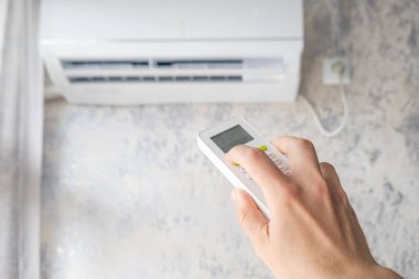 Klimanın ısısını uzaktan kumandayla ayarlıyorum. Sıcak yaz mevsiminde evdeki konfor sıcaklığı için klimayı açan adam. Modern ev teknolojisi