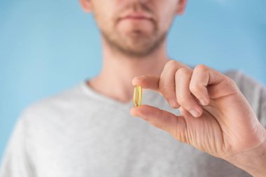 Elinde D vitamini olan kapsüllü bir adam. Balık yağı ile besin takviyesi. Sağlık desteği ve tedavi konsepti. Seçici odak