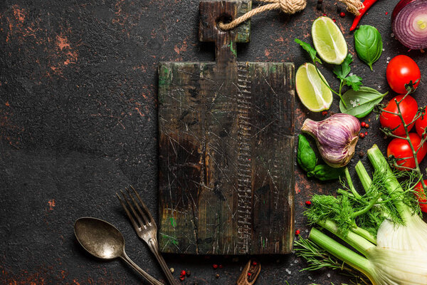 Vegan food cooking background. Fresh vegetables, mushrooms, spices and herbs with cutting board on black stone table. Top view with copy space. Vegan food concept