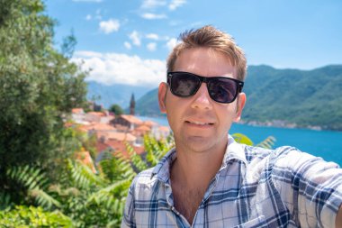 Güneş gözlüklü mutlu adam Karadağ 'ın Kotor Körfezi' nde selfie çekiyor. Erkek turist yaz tatilinde eğleniyor. Gülümseyen adam tatilde eğleniyor, dışarıda kameraya bakıyor. Seyahat ve teknoloji
