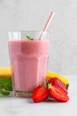 Çilekli ve muzlu smoothie veya bir bardakta milkshake, saman, taze böğürtlen ve beyaz arka planda nane. Yaz ferahlatıcı içecek. Dikey yönelim