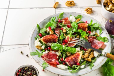 Beyaz fayanslı tabakta roka, peynir ve ceviz ile nefis incir ve prosciutto salatası. sağlıklı diyet yemekleri. 