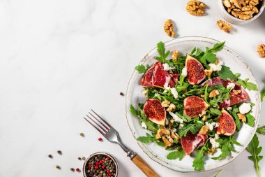 İncirli salata, prosciutto, roka, peynir ve beyaz fayanslı çatallı ceviz tabağı. sağlıklı diyet yemekleri. Kopyalama alanı olan üst görünüm