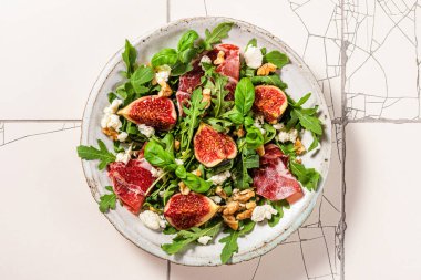 Beyaz fayanslı bir tabakta incirli salata, prosciutto, roka, peynir ve ceviz. sağlıklı diyet yemekleri. en üstteki görünüm