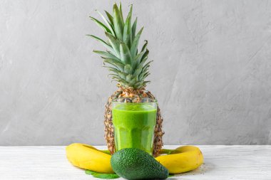 Ispanak, ananas, muz ve avokadodan yapılmış bir bardak yeşil smoothie ve gri arka planda taze meyve ve chia tohumları. Sağlıklı diyet içeceği.