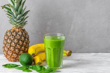 Ispanak, ananas, muz ve avokadodan yapılmış taze meyve ve fotokopi alanı olan gri arka planda chia tohumlarıyla dolu bir bardakta taze yeşil smoothie. Sağlıklı diyet içeceği.