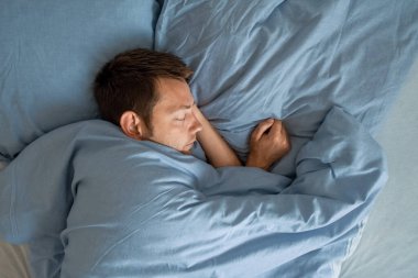Sabahları yatakta uyuyan adam yatak odasındaki sağlıklı yaşam için dinleniyor. Yorgun bir erkek uyuyor ya da otelde rüya görüyor. Üst görünüm.