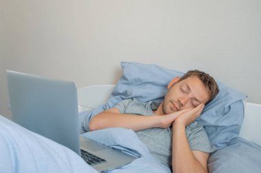 Genç beyaz adam dizüstü bilgisayarın önünde uyuyakaldı. Erkek serbest yazar sabahları dizüstü bilgisayarın arkasında uyuyor. Evden uzakta çalışan bir tasarımcı. Kablosuz teknoloji kavramı