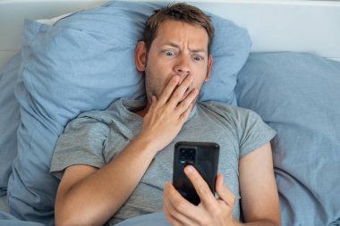 Akıllı telefondan haberleri okuyan yakışıklı bir adam. Sabahları yatakta üzgün bir ifadeyle. Adam cep telefonundan gelen kötü haberlere hayret ediyor, telefonu tutuyor ve ekrana bakıyor..