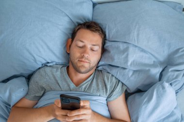 Yakışıklı adam sabah internette cep telefonu kullanıyor, sosyal medyayı kontrol ediyor ve haberleri okuyor. Gadget bağımlılığı. Teknoloji konsepti.
