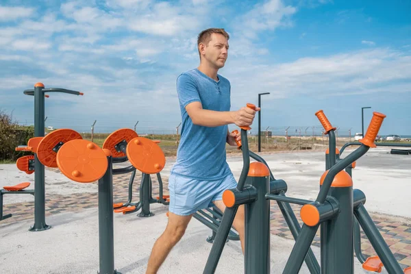 Young male doing cardio workout exercises on elliptical trainer in a street gym. Active man exercising at outdoor gym. Fitness, sport, exercising, training, workout and lifestyle concept.