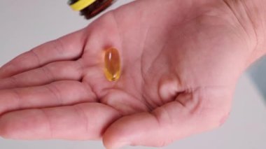 Adam balık yağı kapsüllerini omega 3 ile dolduruyor. İlaç şişesinden D vitamini. Besin takviyesi. Sağlık desteği ve tedavi konsepti. Kapat.