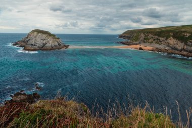 Santander, Cantabria, Kuzey İspanya 'daki Covachos plajlı, kayalık adalı ve bulutlu bir günde kumlu tükürük kaplı Castro Adası' nın kasvetli manzarası. Tatillerde popüler seyahat