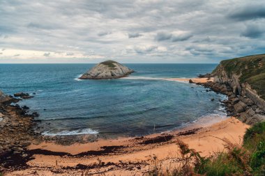 Santander, Cantabria, Kuzey İspanya 'da Playa de Covachos plajı. Kayalık adası ve bulutlu bir günde kum tükürüğü. Tatillerde popüler seyahat