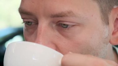 Köpüklü kahve kapuçino ya da köpüklü dudaklı bir kahvehanede latte içen bir adam. Kafkasyalı erkek, sabah içkisini kaldırımdaki kafede içiyor. Kapatın. Lezzetli sıcak içecek.