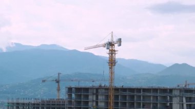 Vinçler, gün batımında arka planda dağlarla birlikte şehrin inşaat sahasına çok katlı bir ev inşa ederler. Yeni binalar inşa etme sanayisi. Endüstriyel kavram.