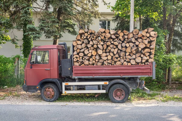 Dump truck with a body full of firewood. Truck loaded with stack of wooden logs to delivery for heating season. Firewood for the stove during the winter cold.