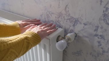 Closeup of man warming his hands in yellow sweater on the heater at home during cold winter days. Male getting warm up his arms over radiator. Concept of heating season or cold weather.