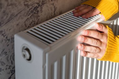 Adam soğuk ve güneşli kış gününde ellerini radyatörde ısıtıyor. Erkek, ısıtıcı yüzünden kollarını ısıtıyor. Isınma mevsimi ya da soğuk hava kavramı.