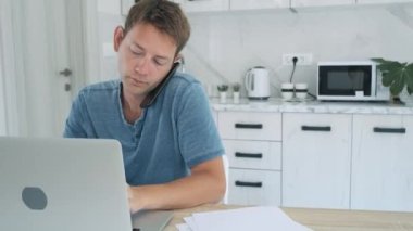 Ciddi bir tüccar evde dizüstü bilgisayarla çalışırken telefonla konuşuyor. Borsada çalışan profesyonel erkek borsacı ve akıllı telefon ve bilgisayarlı kripto para birimi.