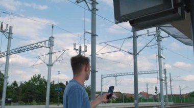 Akıllı telefonlu bir adam tren istasyonundaki tren saatine bakıyor. Cep telefonlu bir erkek gezgin zaman çizelgesine bakar ve mobil uygulamadan online bilet ayırtır. Demiryolu ile seyahat