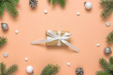 Noel hediyesi kutusu, köknar dallarından, kozalaklardan ve şeftali rengi arkaplanda Noel süslerinden yapılmış çerçevede. Düz yatıyordu. Üst görünüm.