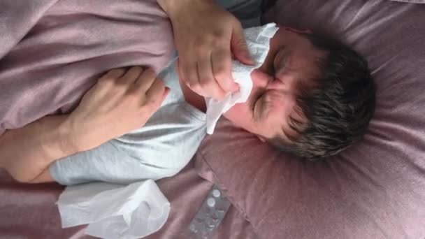 インフルエンザ 風邪またはウイルスが鼻水を吹いて病気の原因となるアジアの若者は 熱が風邪を引き 自宅のベッドに横たわって組織でくしゃみをした トップ表示 — ストック動画
