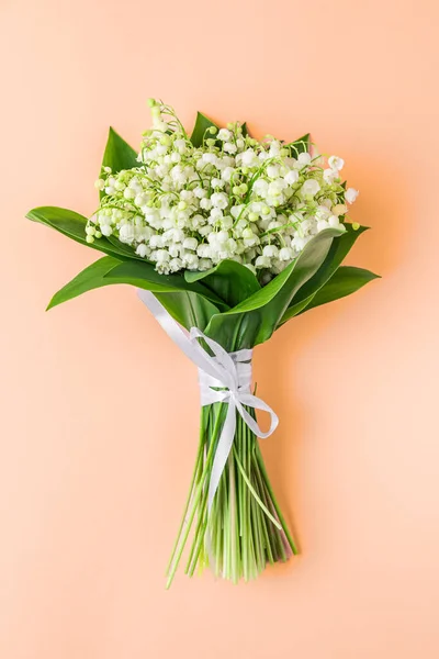 Lily of the valley flowers bouquet on peach color background. Womens day, Valentines day card. Top view. Flat lay. Vertical orientation. Trendy color 2024.