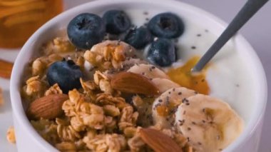 Bir kase yulaf lapası yoğurt, muz, yabanmersini, chia tohumu, bal ve fındıklı sağlıklı kahvaltı için beyaz arka planda. Kapatın. Diyet yemek.