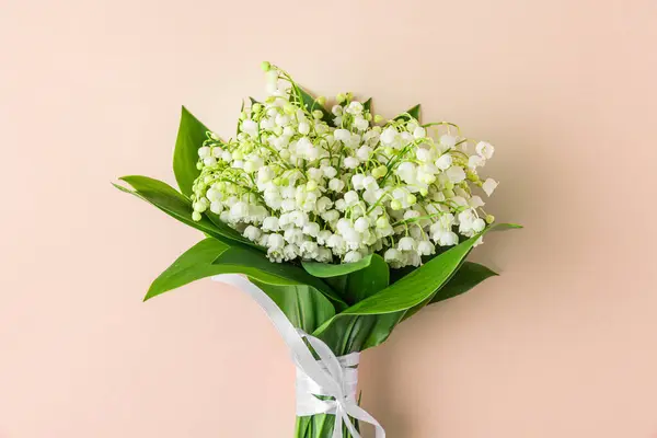 Lily of the valley flowers bouquet on peach color background. Womens day, Valentines day card. Top view. Flat lay. Trendy color 2024.