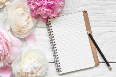 Pastel pembe ve beyaz şakayık çiçekleri, beyaz ahşap zemin üzerinde kalem olan çizgili kağıt defter. Düğün davetiyesi. Model yap. Düz yatıyordu. Kadın Günü, Anneler Günü planı..