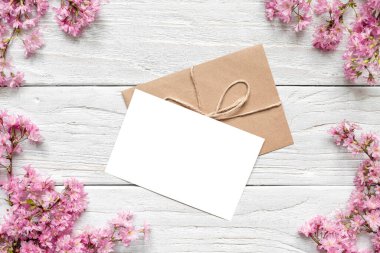 Bahar pembesi çiçeklerinden yapılmış çerçevedeki boş tebrik kartı beyaz ahşap arka planda çiçek açıyor. Model yap. Düz yatıyordu. Üst Manzara. Kadınlar Günü, Anneler Günü, Düğün ya da fotokopi alanı ile yıldönümü davetiyesi.