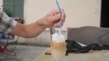 Kahve dükkanında bir pipetle kremalı buzlu latte kahvesi içen adam. Soğuk yaz içeceği. Sabah kahve molası..