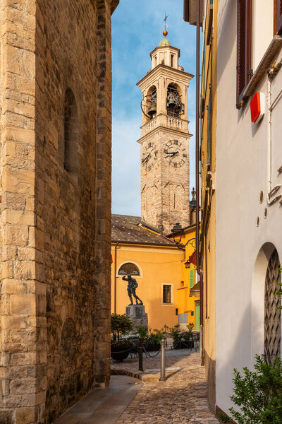 View on medieval town square with church Chiesa Santo Stefano with tower from narrow street in Lenno comune on Como lake, Lombardy, Italy. Vertical orientation. Popular travel and tourist destination