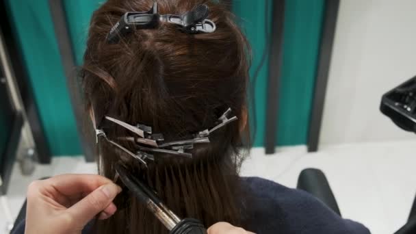用胶囊和加热工具将头发在美容院中混入 理发师为黑发女人理发 用角蛋白进行头发伸展 增加头发体积 专业护理 — 图库视频影像