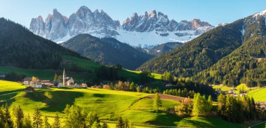 Santa Maddalena köyünün güneşli manzarasının panoramik manzarası, gün doğumunda karla kaplı Geisler dağlarına karşı, Val Di Funes Dolomites dağlarında, Güney Tyrol, İtalya. İtalyan Alpleri