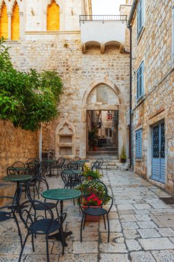 Açık hava restoranındaki eski ortaçağ kasabası Hvar 'ın eski rahat sokağında, dışarıda kafe masaları ve sandalyeler. Hırvatistan' ın Dalmaçya kentinde kimse yok. Dikey oryantasyon. Popüler seyahat ve turizm
