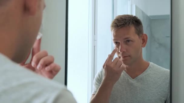 トイレに立って鏡を見た後 顔に保湿クリームを塗った白人ハンサムな若者の反射 毎日の朝のルーチン男性衛生美容手順 — ストック動画
