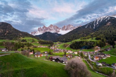 Santa Magdalena köyünün karla kaplı Geisler dağlarına karşı olduğu gün batımı manzarası, Dolomites dağlarındaki Val Di Funes vadisi, Güney Tyrol, İtalya. İlkbaharda İtalyan Alpleri.