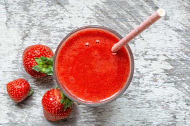 Taze böğürtlenli bir bardakta çilekli smoothie ve beyaz ahşap arka planda saman. Üst Manzara. Sağlıklı yaz içeceği.