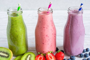 Taze meyve suyu çeşitleri ya da cam şişelerde taze böğürtlenli milkshake ve beyaz ahşap arka planda saman. Kırmızı, yeşil ve mavi şişeler sağlıklı yaz diyeti içecekleri..
