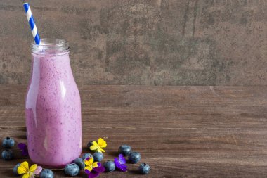 Bir şişe yabanmersinli smoothie ya da taze böğürtlenli milkshake, yenilebilir çiçekler ve kırsal ahşap arka planda saman. Sağlıklı diyet içeceği. Metin için boşluk