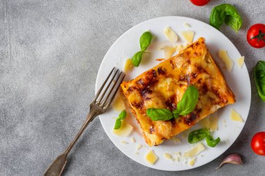 Ev yapımı et lazanyası taze fesleğen, parmesan peyniri ve kiraz domatesli gri arka planda. İtalyan mutfağı. Kopyalama alanı olan üst görünüm. Akşam yemeği için lezzetli yemekler..