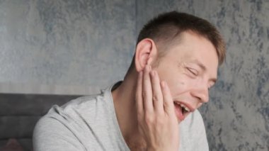 Güçlü diş ağrısı çeken bir adam. Caries, pulpitis, diş apsesi, diş hassasiyeti olan üzgün erkek evde oturuyor ve yanak ağrısına dokunuyor. Diş sağlığı sorunları kavramı. 