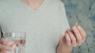 Omega 3 ile kapsül içen adam, bir bardak suyla D vitamini. Balık yağı ile besin takviyesi. Sağlık desteği ve tedavi kavramı.