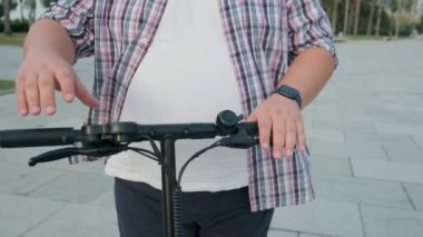 Şişman adam kullanmadan önce e-scooter 'ı kontrol ediyor. Artı boy erkek, elektrikli scooter kiralıyor. Elektrik ve ekolojik şehir ulaşımı. Çevre dostu ulaşım. Sürdürülebilir yaşam tarzı kavramı.